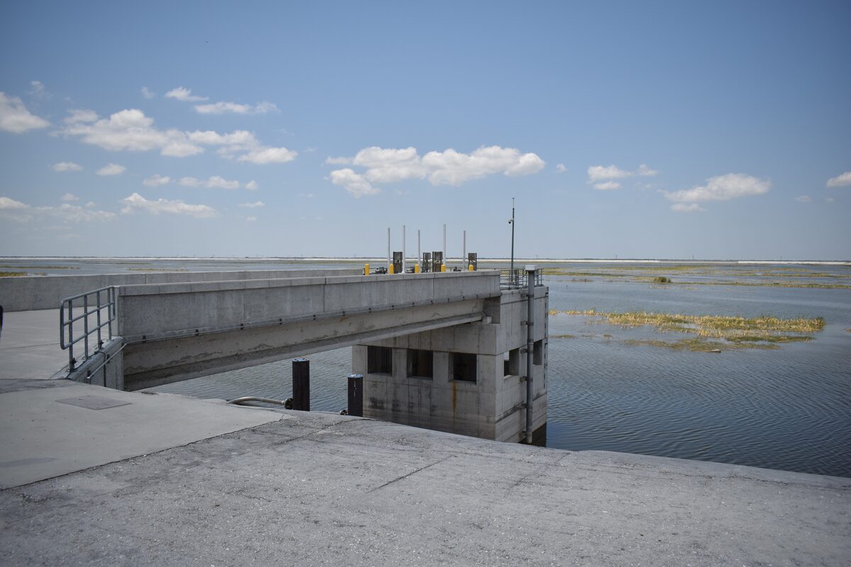 Aerial-adjacent view of a large stormwater treatment area gate structure with rectangular water cells and surrounding green land under a partly cloudy sky.